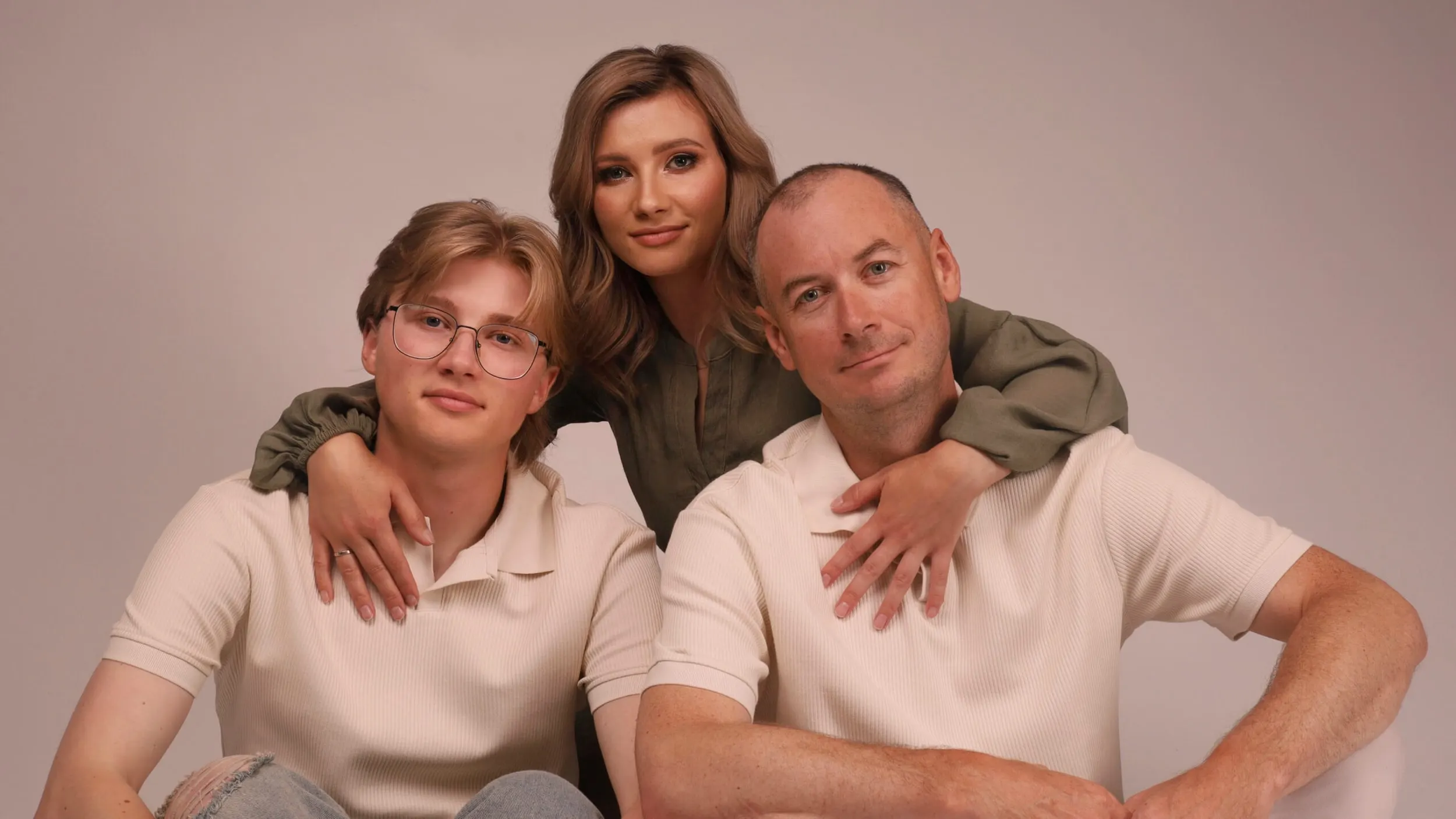 Trois personnes posent ensemble en s’enlaçant ; un portrait horizontal en studio.